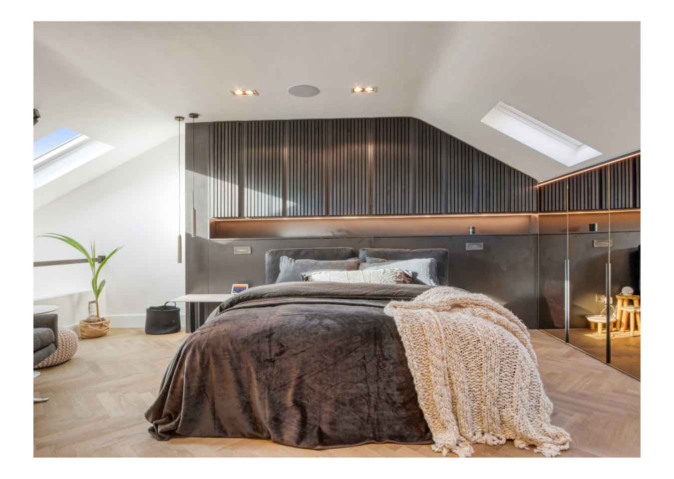 Grey and white bedroom with grey wood panelling above the bed, mirrored wardrobes, a skylight and house plants.