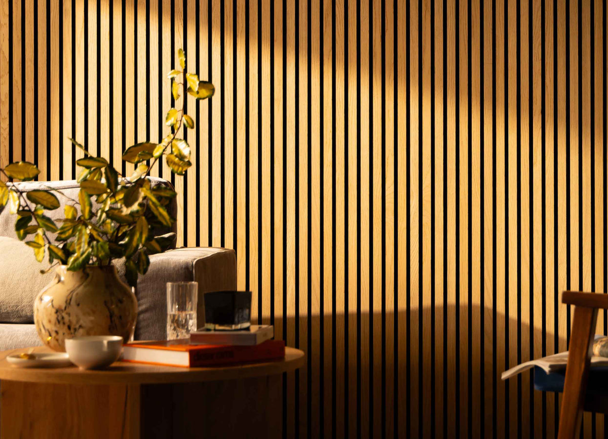 SlatWall Natural Oak panelling in a living room with a grey sofa, wood table, books and a beige marble vase with greenery.