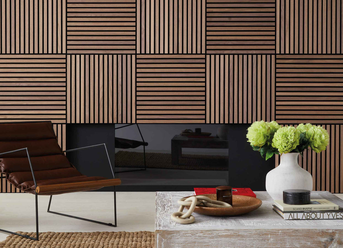 Brown living room featuring wood SlatWall panels, a brown leather chair, white coffee table, books, candles and green flowers.