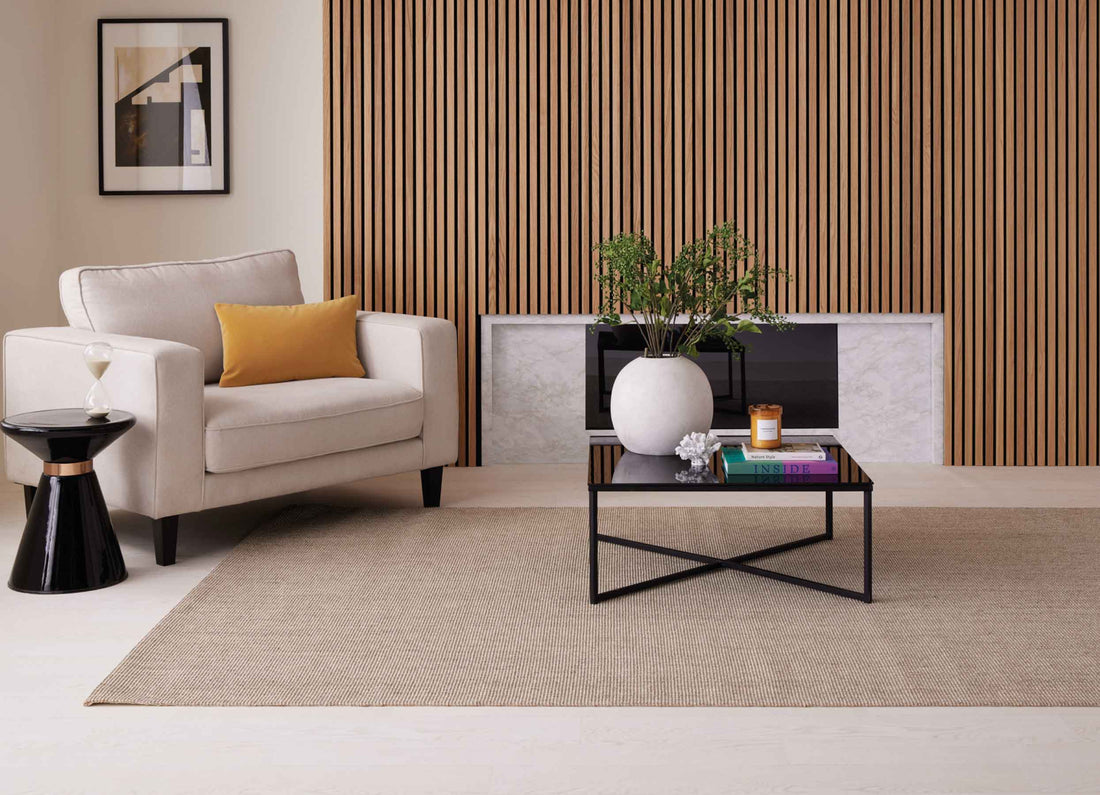 Living room wall panelling idea with oak wood panels above a fireplace, a cream chair, black tables and amber accessories.