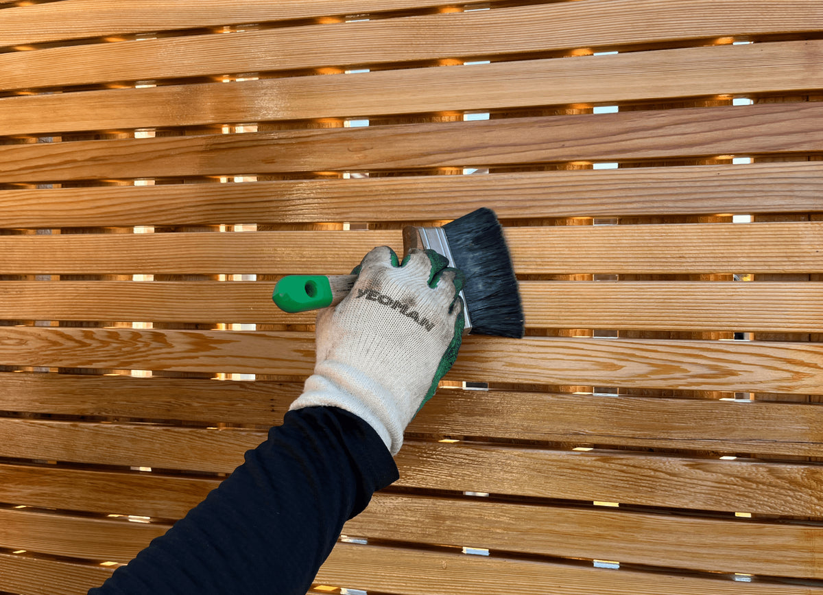 Hand holding paint brush applying UV protection oil onto out Cedar wood panels