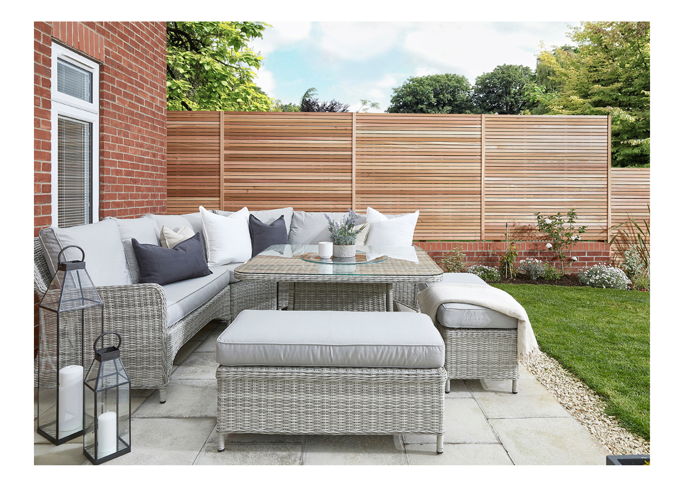 Outdoor living room with a grey corner sofa and table next to Cedar fence panels.