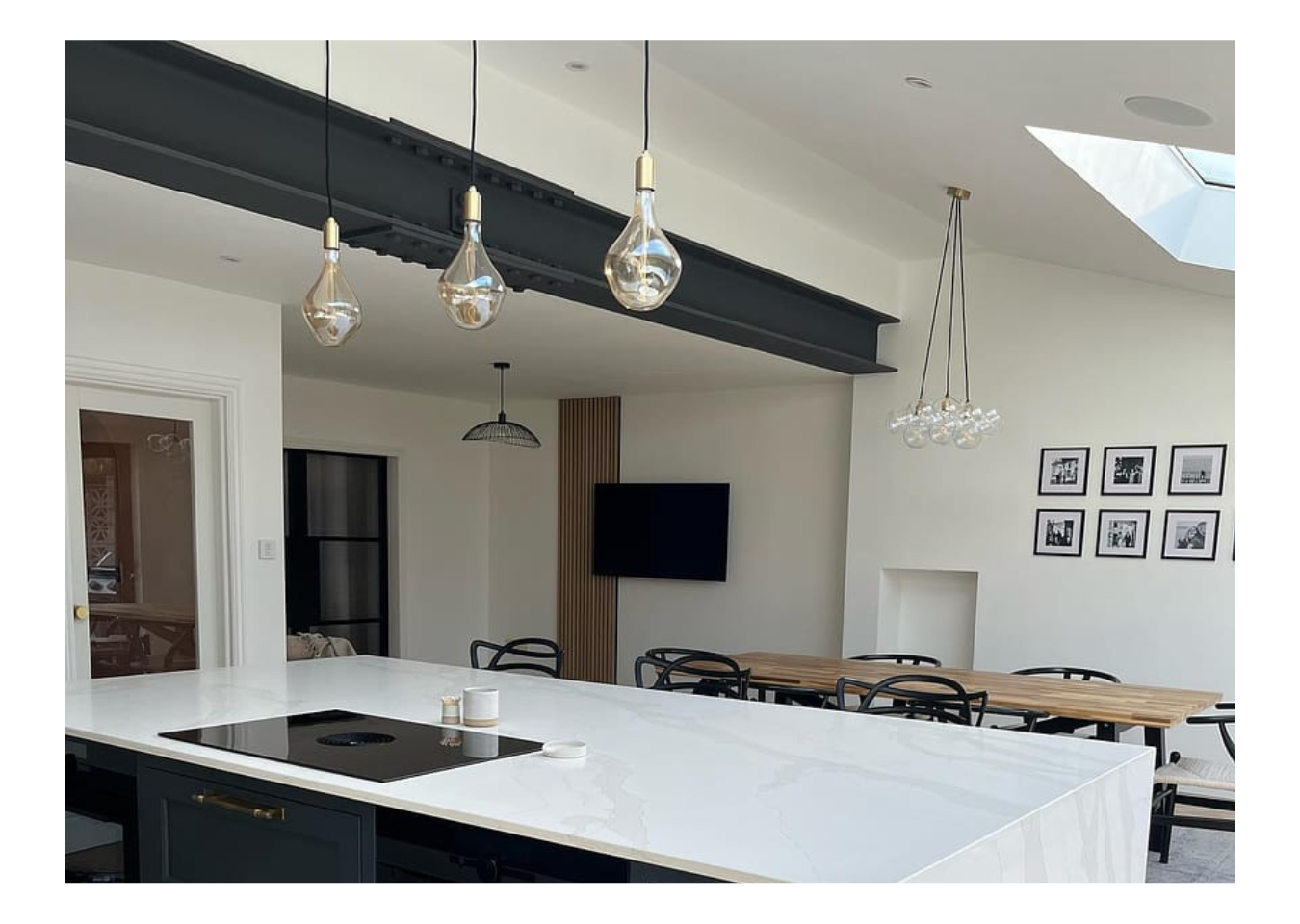 White and black open-plan kitchen and dining area featuring a single brown SlatWall panel behind a TV next to a wood table.